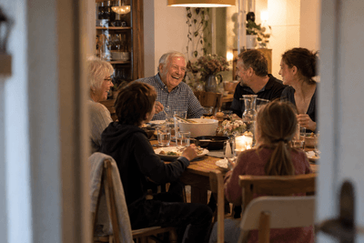 Älterer Mann lacht beim Abendessen mit seiner Familie an einem großen Holztisch
