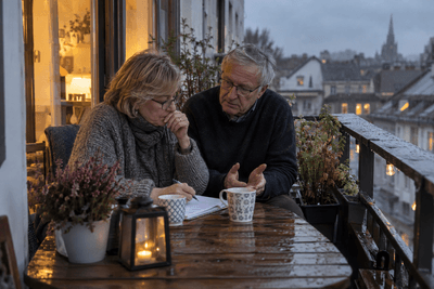 Älteres Paar bespricht in der Abenddämmerung auf dem Balkon etwas über einem Notizblock, sie schreibt mit