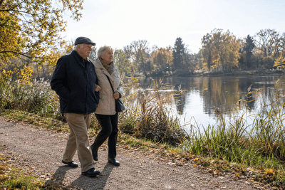 Älteres Ehepaar spaziert Arm in Arm an einem Seeufer im Herbst